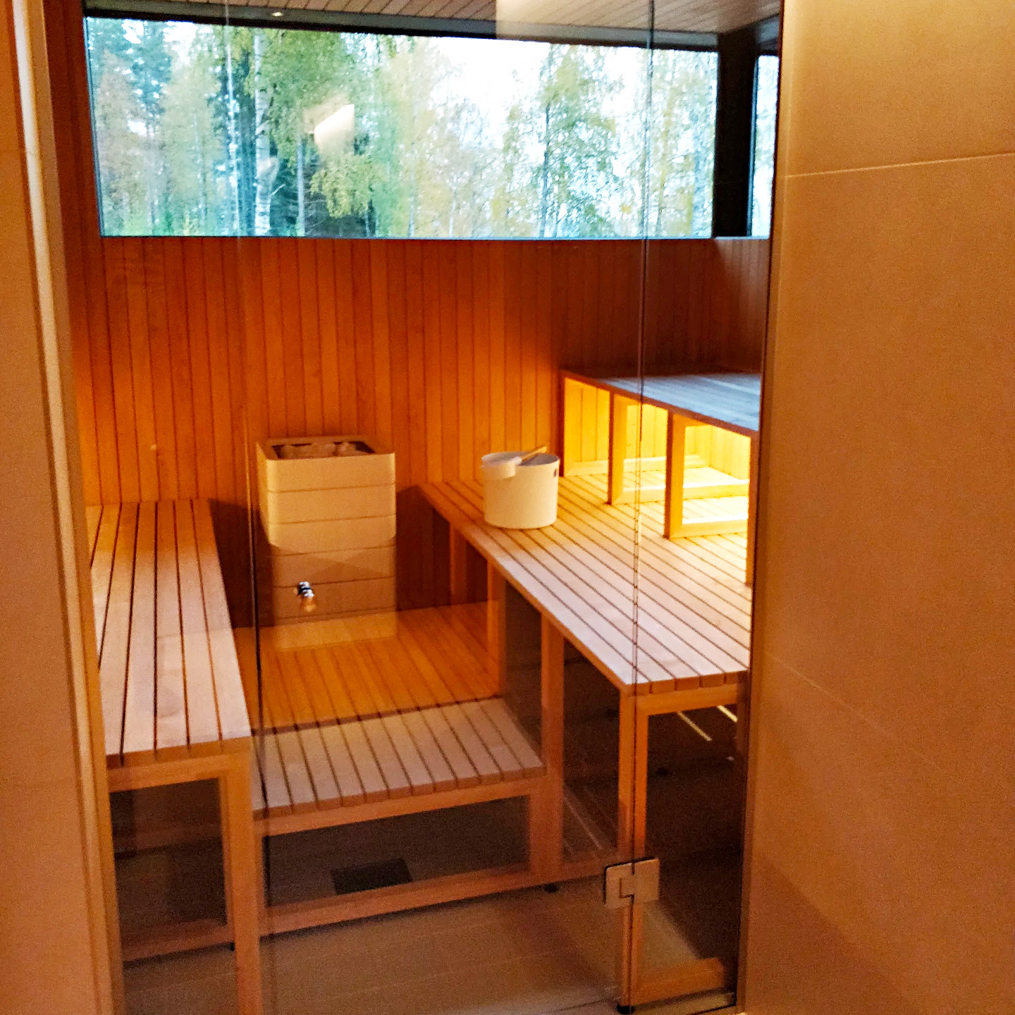 Tunnelmallinen sauna jossa on kiuas keskellä ja lasiseinät. Saunan on rakentanut Rakennuspalvelu RI-LI Mikkelissä